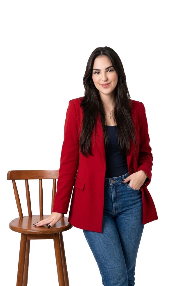 Laura Trindade, psicóloga, em pé com blazer vermelho, a mão apoiada em um banco de madeira.